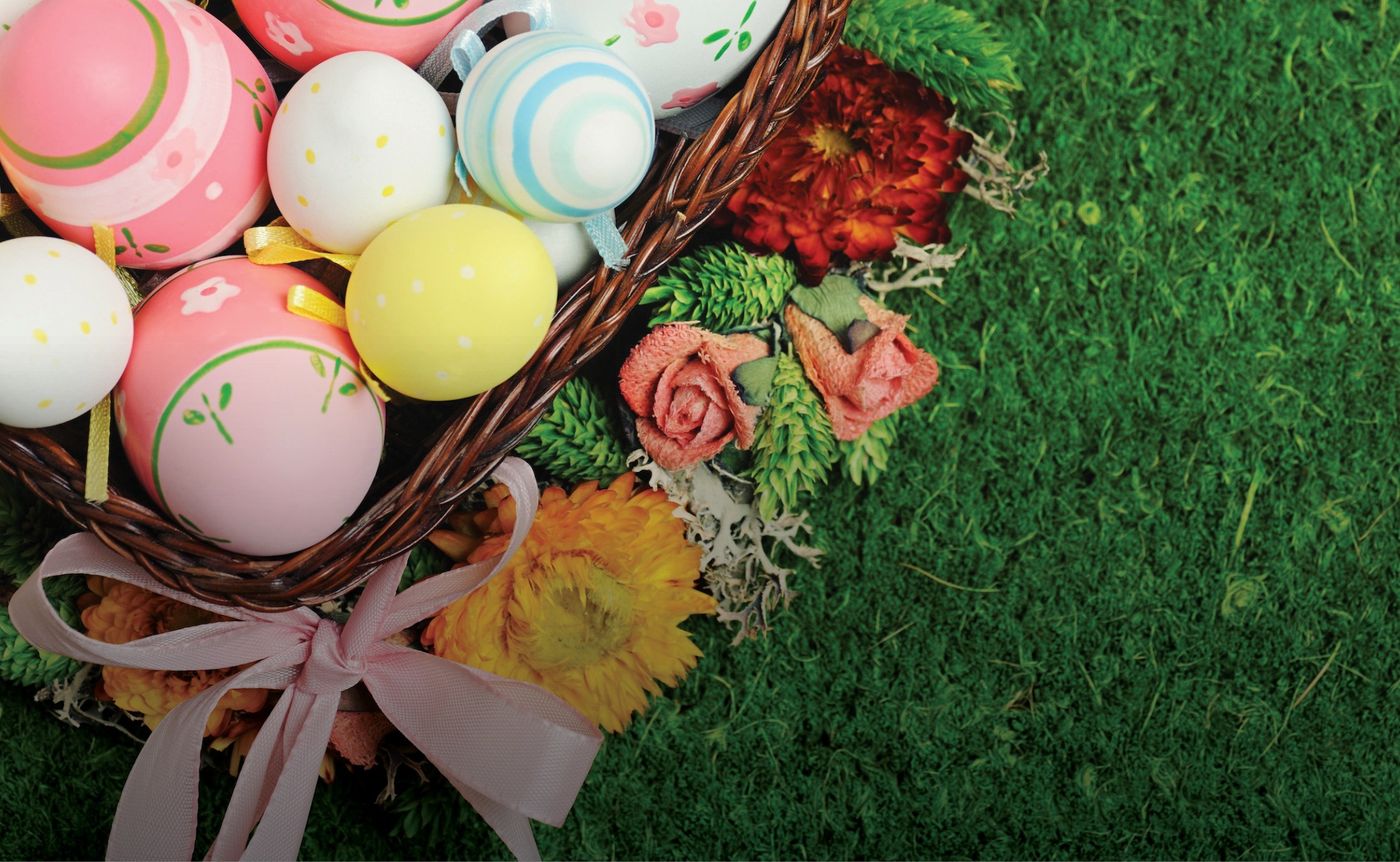 Cesto de Páscoa com ovos decorados em tons pastel, flores e laço rosa sobre relva verde, numa imagem alusiva à celebração da Páscoa na Quinta da Carlota.