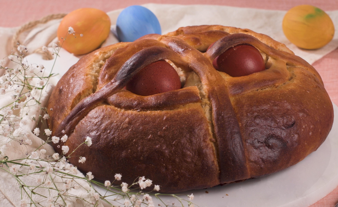 Folar de Pascua tradicional con huevos cocidos, en una fuente, con huevos de colores al fondo.