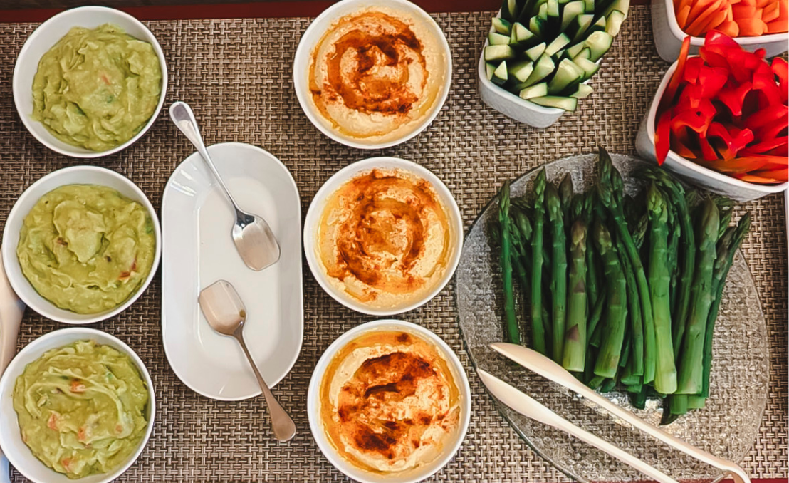 Mesa con snacks saludables, incluyendo espárragos, verduras cortadas y salsas