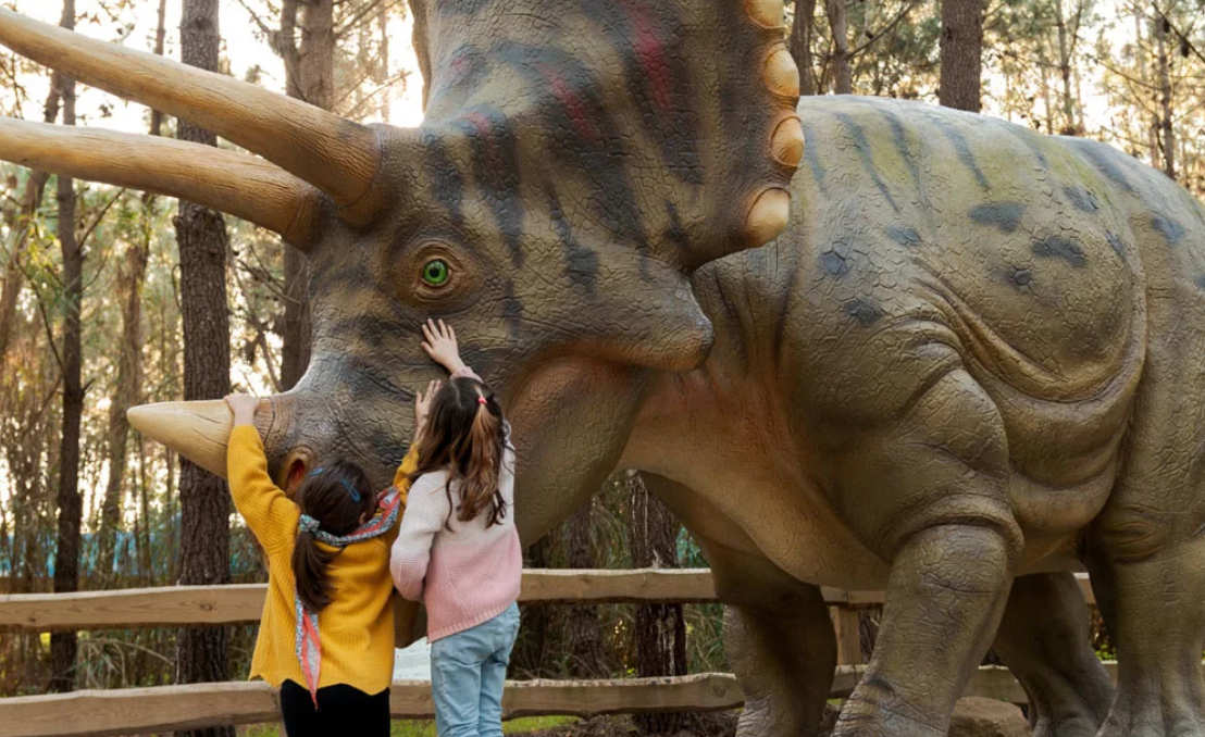 Niños tocando un modelo de dinosaurio en un parque temático