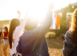 Jovens a dançar e a levantar os braços num festival de verão ao ar livre ao pôr do sol