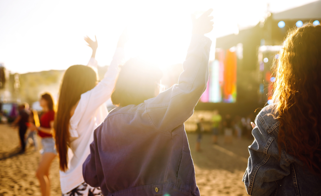 Jovens a dançar e a levantar os braços num festival de verão ao ar livre ao pôr do sol